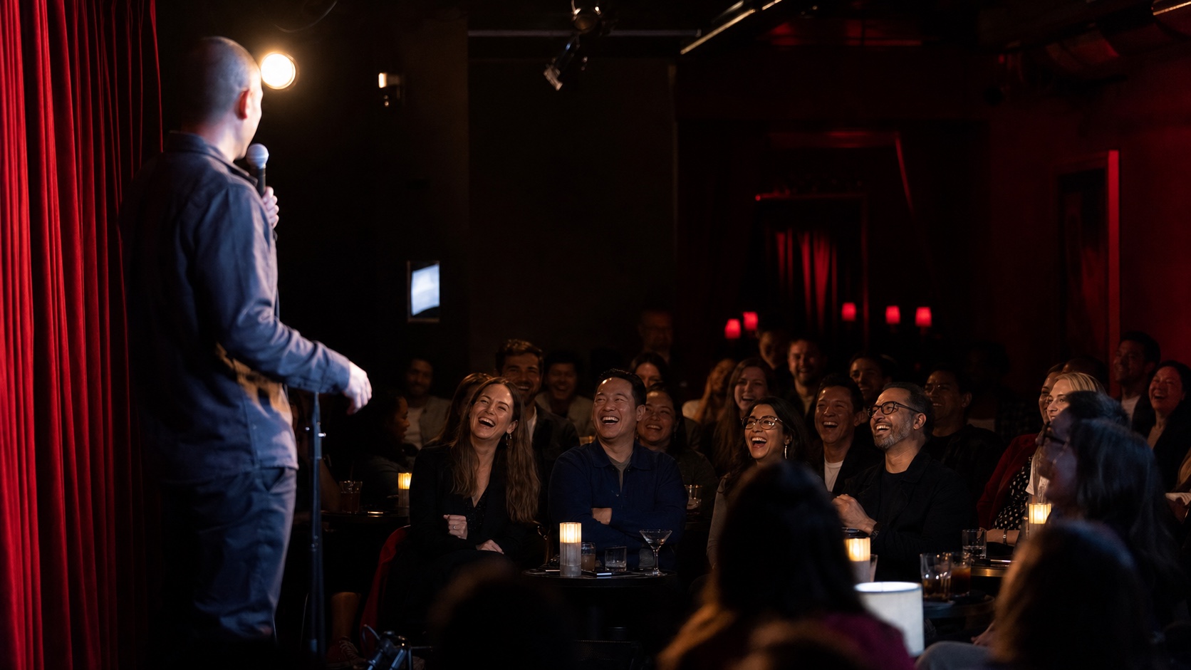 A stand-up comedian performing in a dark Los Angeles club under a single spotlight